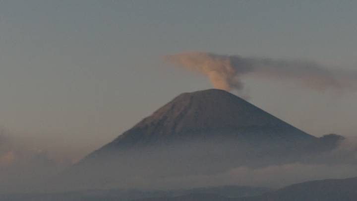 Distant volcano emits plume of smoke above low clouds at dawn