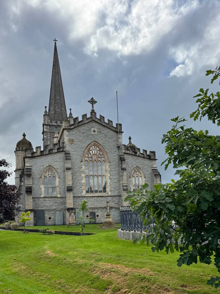 Stone-walled church with pointed spire framed by leafy trees
