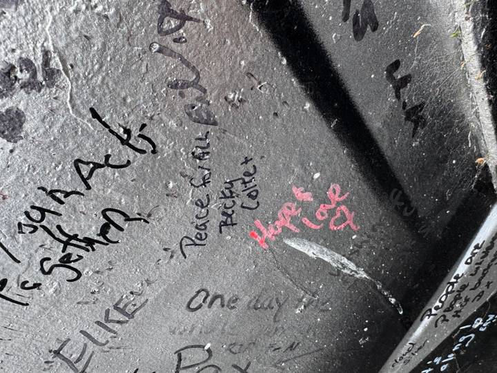 Close-up of graffiti messages and signatures on a dark mural wall