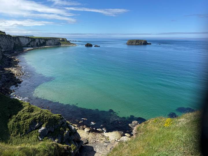Turquoise sea laps against rugged cliffs and a small offshore island under a blue Irish sky.
