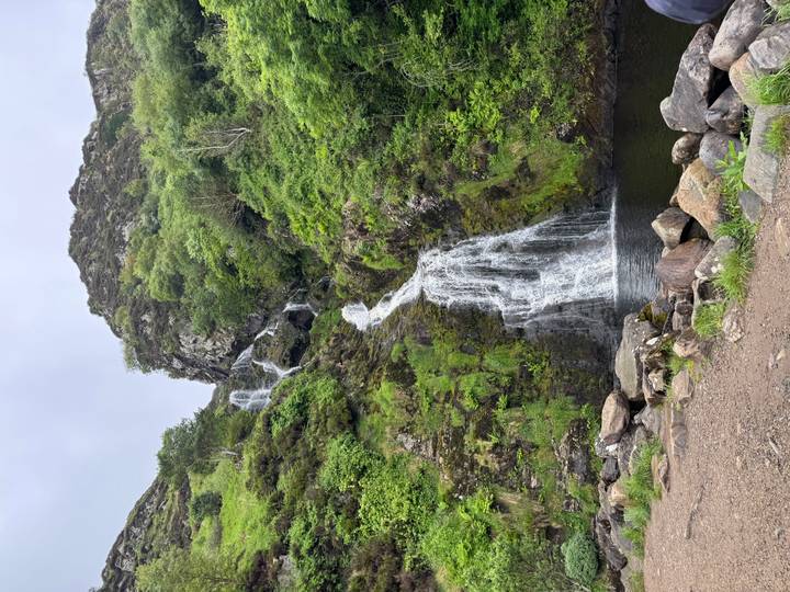 Thin waterfall cascades down a mossy, rocky cliff into a small pool surrounded by boulders.