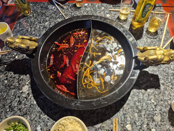 Traditional Chinese hot-pot divided pot with red chili broth and clear mushroom broth on a granite table.