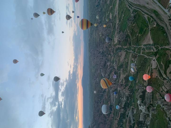 Dozens of hot-air balloons drift above the surreal valleys of Cappadocia at dawn.