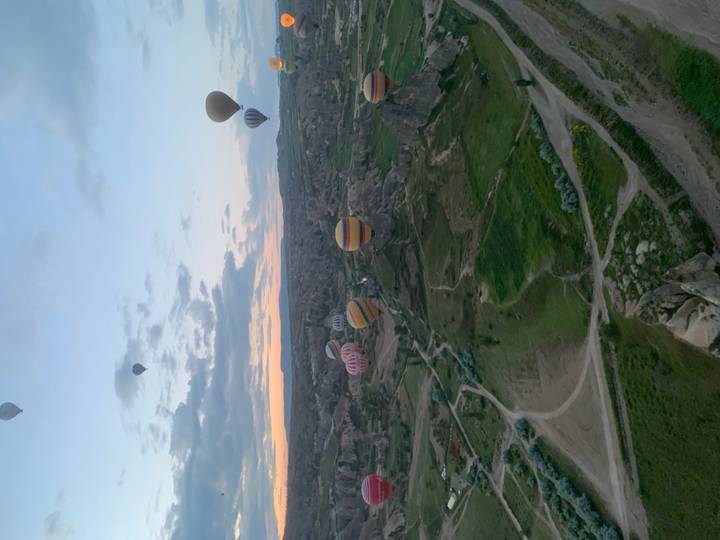Colorful balloons float above rugged rock valleys under a pastel dawn sky.