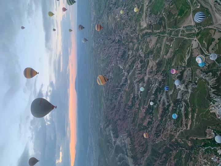 Wide aerial view of Cappadocia’s dramatic landscape dotted with dozens of hot-air balloons.