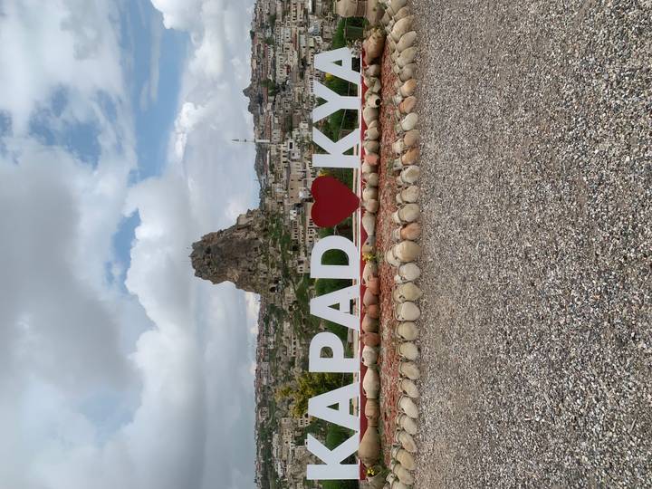 Large white letters spelling Cappadocia with a heart sit before the towering Uchisar Castle rock.