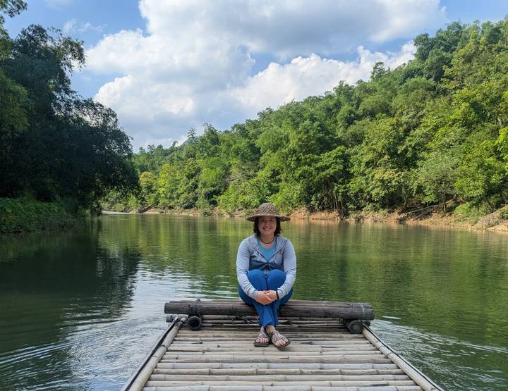 Woman sitting cross-legged on a small bamboo raft floating on a serene jungle river.