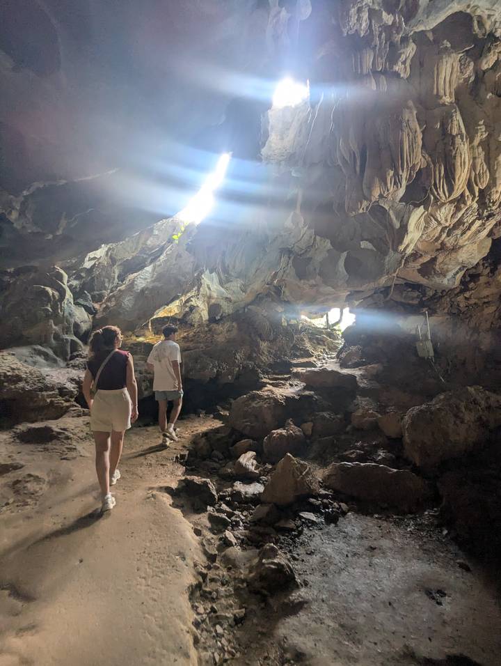 Travelers exploring the interior of a limestone cave with sunlight streaming through an opening.
