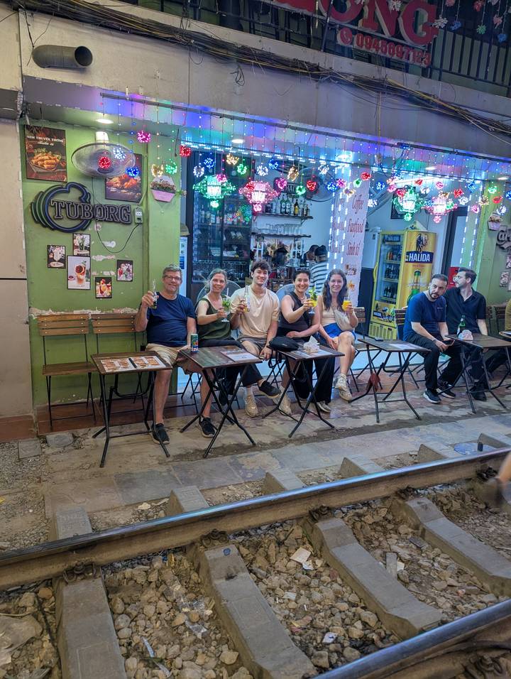 Group of friends sitting at small outdoor tables on a Hanoi street drinking beer at night.