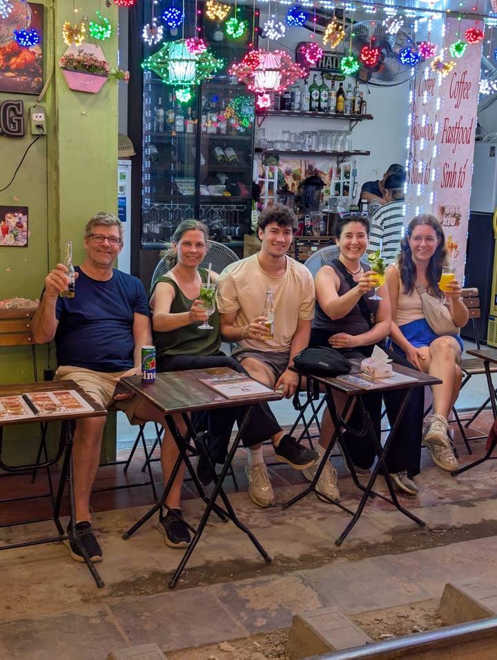 Group of five people sitting at small tables on a Vietnamese street enjoying colorful drinks and beer.
