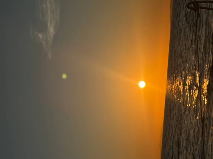 Golden sun setting over a calm sea, its reflection shimmering on the water’s surface.