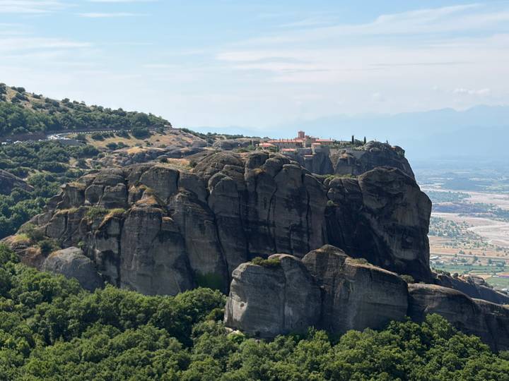 Dramatic rock pillars crowned by an ancient monastery overlook a lush valley in Meteora, Greece.