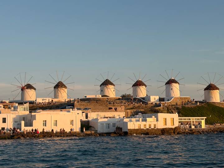 Iconic white windmills of Mykonos line the hilltop, glowing in golden evening light above the sea.
