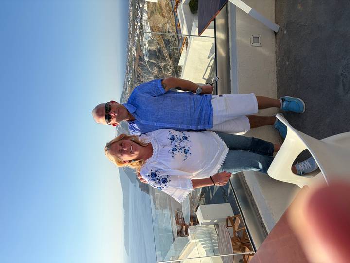 Couple stands on a balcony overlooking Santorini’s caldera and whitewashed villages.