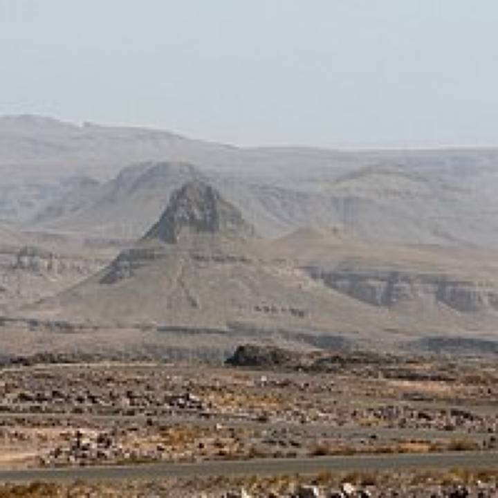 Low-resolution image of an isolated mesa rising from a barren rocky plateau.
