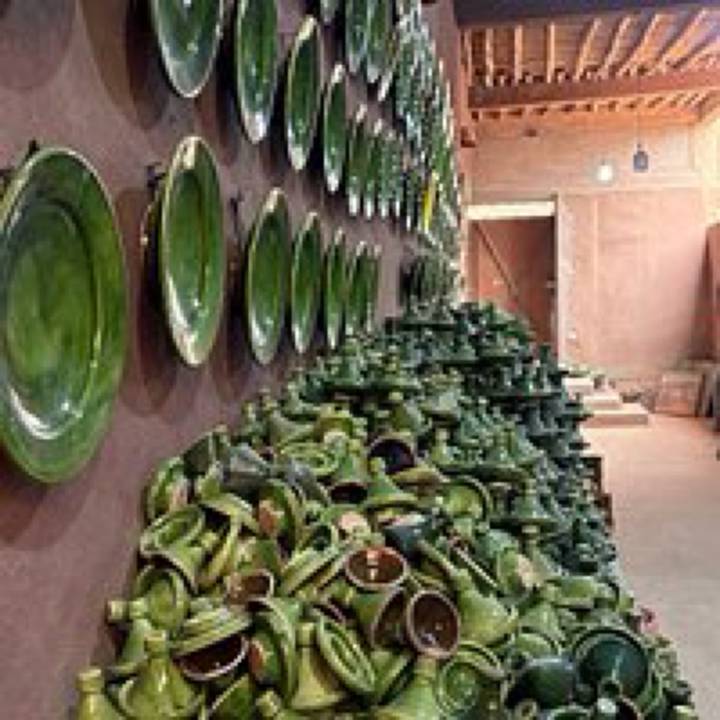 Blurry display of stacked green pottery against a terracotta wall in a workshop.