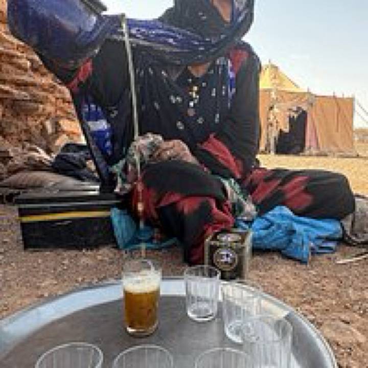 Pixelated image of a traditionally dressed woman serving tea in a desert camp.