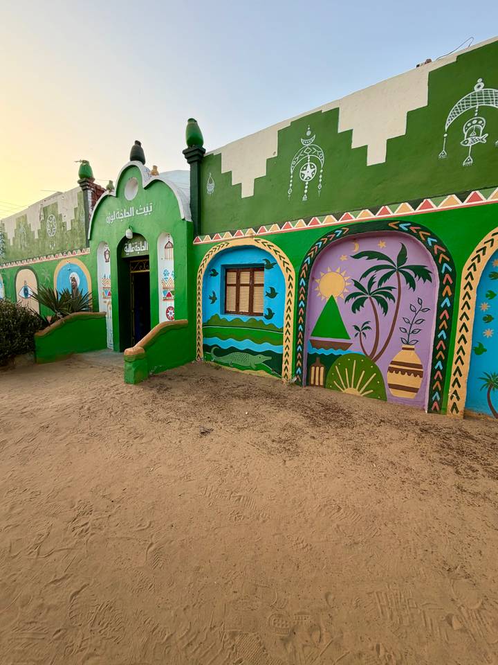 Colourful Nubian-style murals depicting nature and village life decorate a green adobe house.
