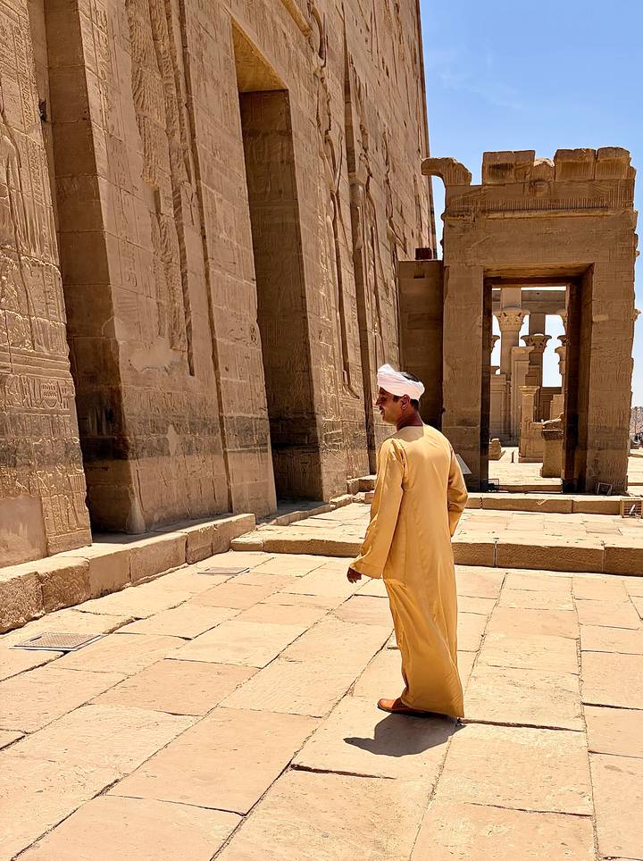 Man in traditional galabeya walks past hieroglyph-covered sandstone columns at Philae Temple.