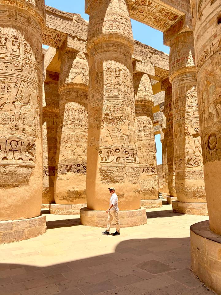 Gigantic hieroglyph-covered columns of Karnak Temple soar above a lone visitor.