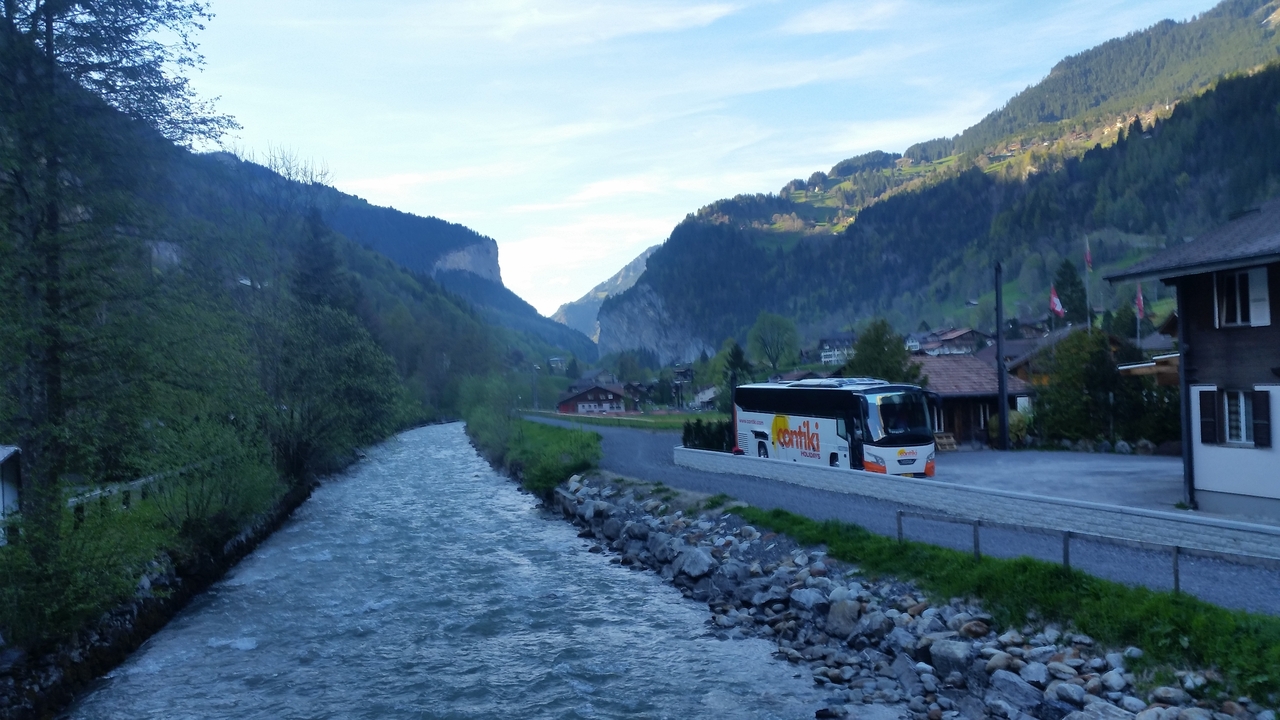 Rivière coulant dans une vallée montagneuse avec un bus touristique garé à proximité.