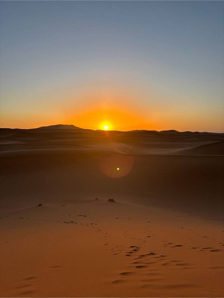 The sun peeks over rolling sand dunes casting a warm glow across the silent desert.