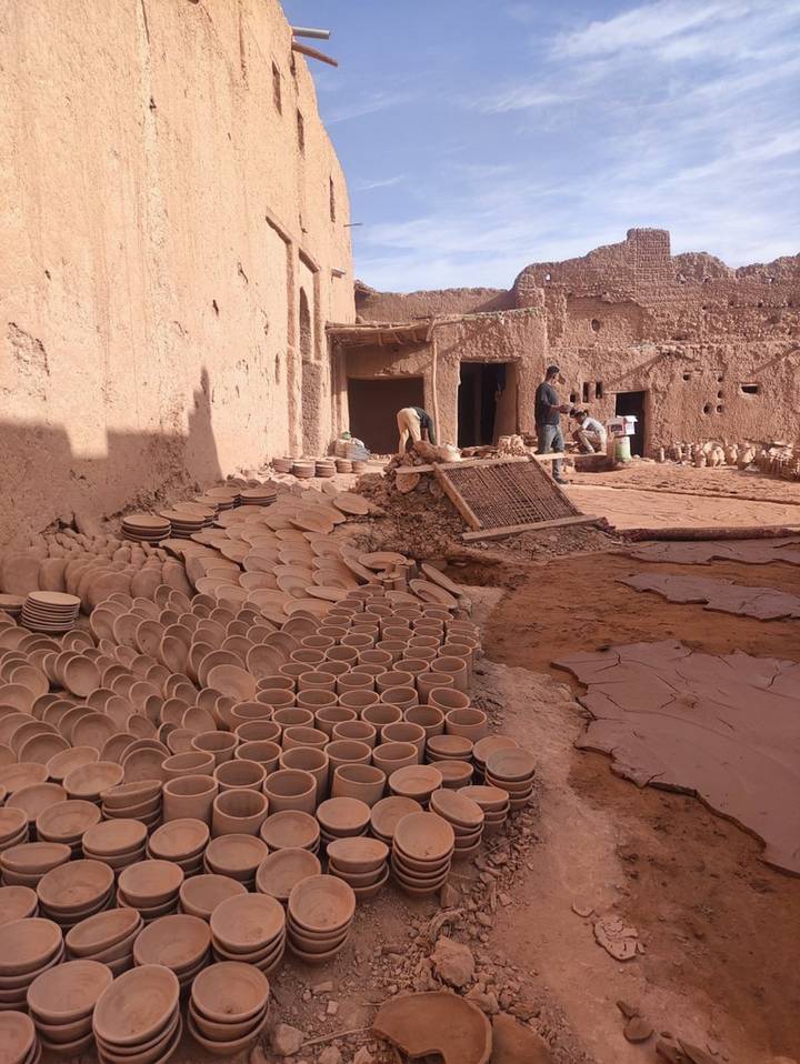 Artisans craft and dry stacks of clay plates in a sun-baked earthen pottery yard.