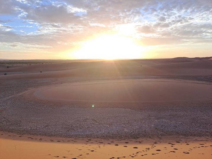 Low sun bursts over vast cracked desert flats and gentle dunes stretching to the horizon.