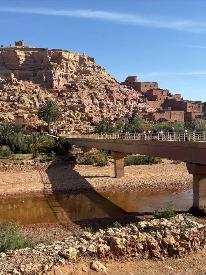 Visitors cross a modern bridge toward the fortified hillside village of Ait Ben Haddou.
