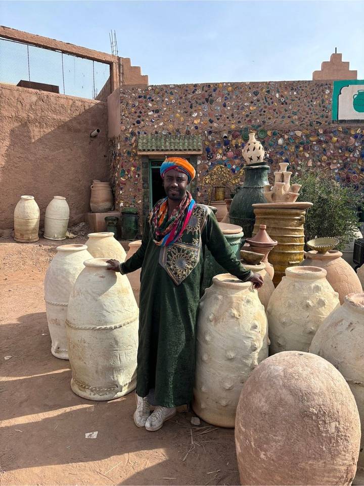 Local man in colourful turban stands among large handcrafted clay jars outside a pottery workshop.