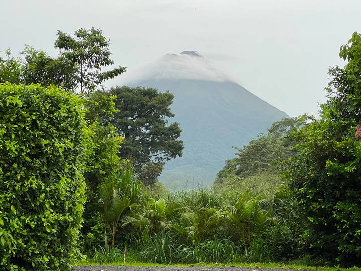 Dramatic view of cloud-shrouded Arenal Volcano framed by dense tropical greenery.