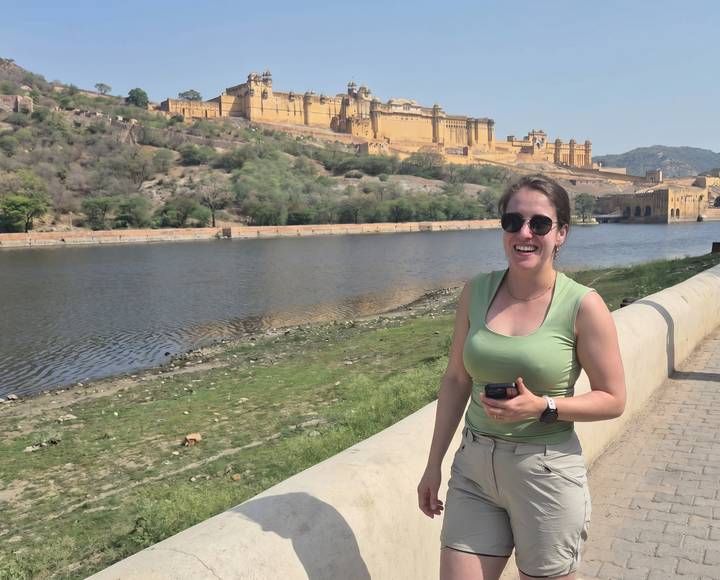 Female traveler smiling beside a stone balustrade overlooking the lake and towering Amber Fort in Rajasthan.