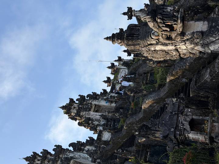Ornate stone temple complex rising against a bright blue Balinese sky.