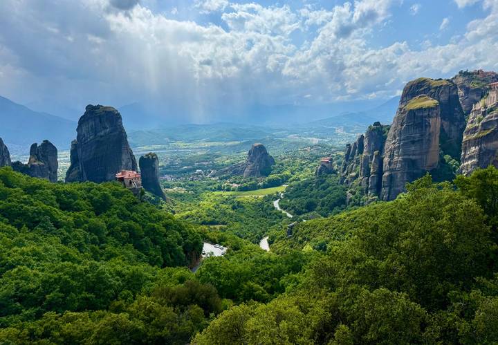 Panoramic vista of lush Meteora rock pillars and monasteries under dramatic sky.
