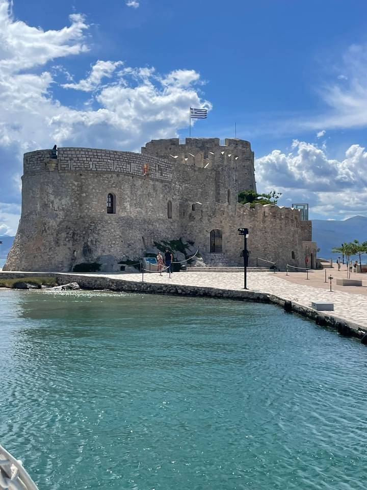 Stone sea fortress rising from turquoise waters under a bright scattered cloud sky.