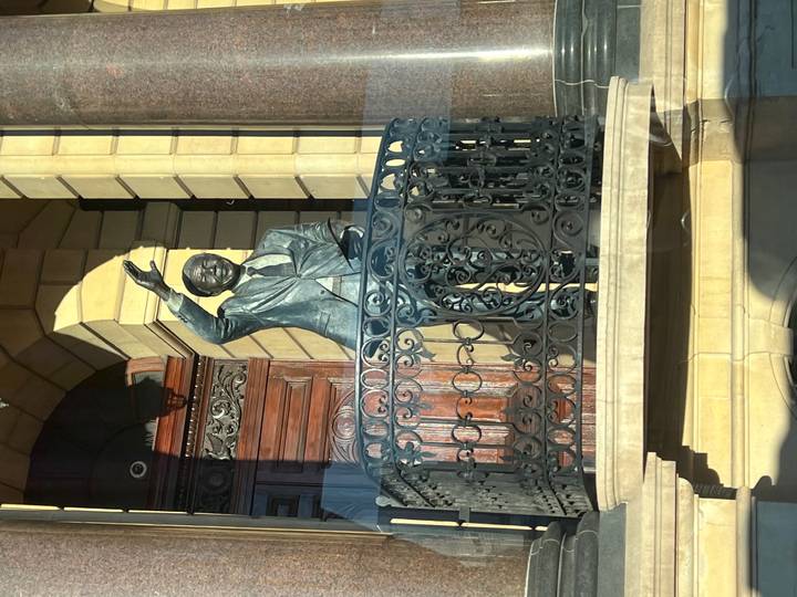 Bronze statue of Nelson Mandela waving from an ornate balcony in front of a historic building