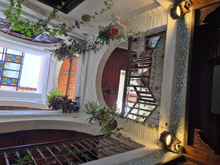 Looking up inside a traditional Moroccan riad courtyard with white stucco arches, hanging plants and a skylight.
