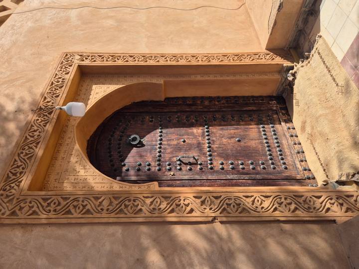 Ornately carved wooden door with decorative arch and brass studs set in an earthen wall.