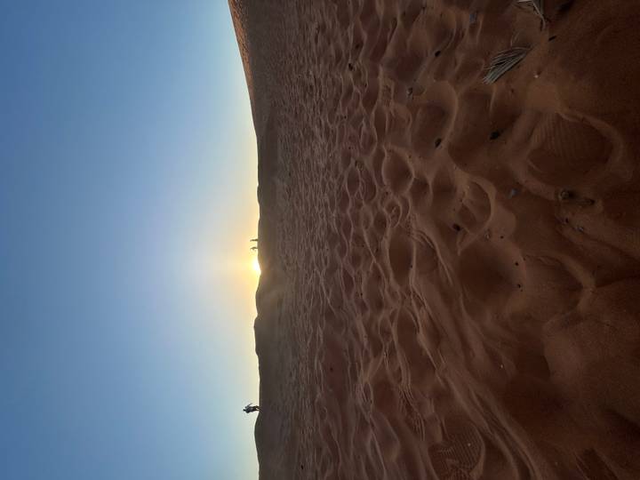 Low sun setting behind desert dunes casting a soft glow over rippled sand in the foreground.