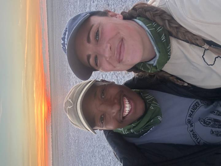 Smiling couple take a selfie on a salt pan at colorful sunrise with orange sky on the horizon.