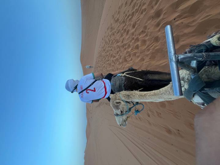 Camels and riders continue over a desert ridge under a deepening twilight sky.