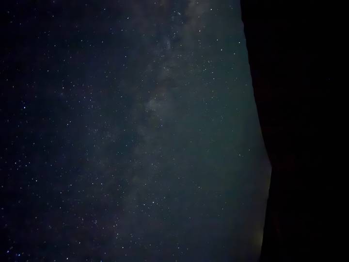 Star-filled night sky with faint Milky Way above a dark desert horizon.