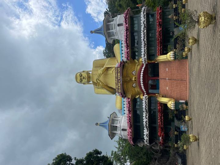 The towering golden Buddha statue at Dambulla Golden Temple rises against a dramatic cloudy sky.