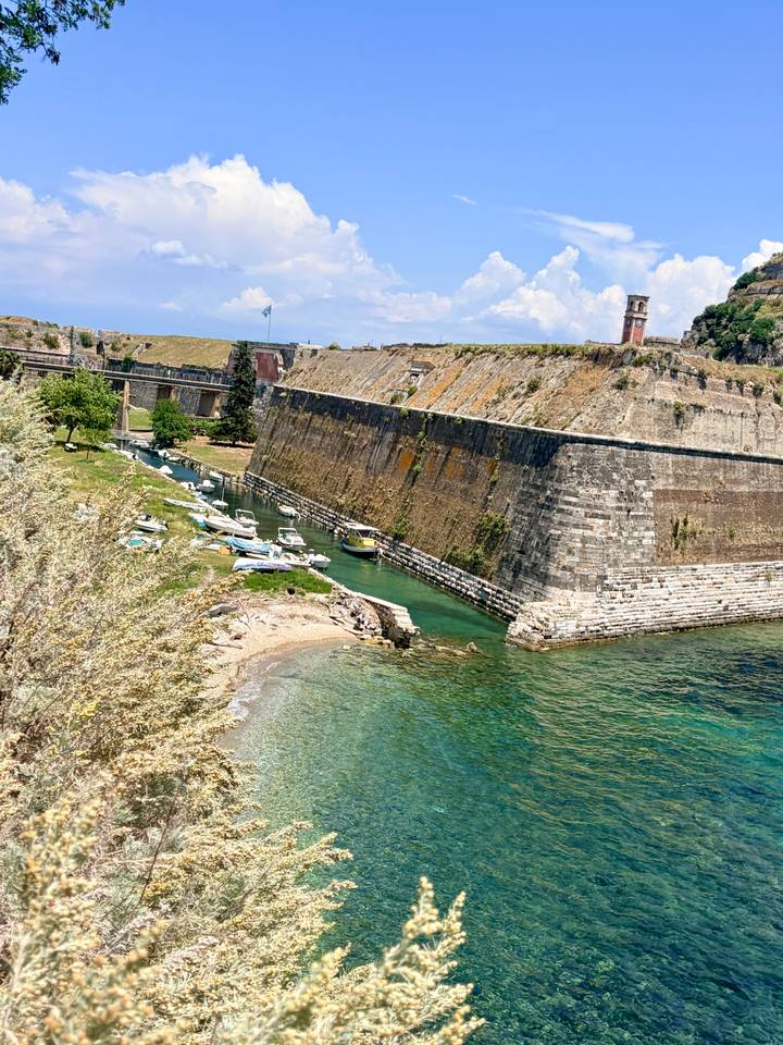 A clear turquoise inlet and small beach nestle beside towering stone fortress walls.