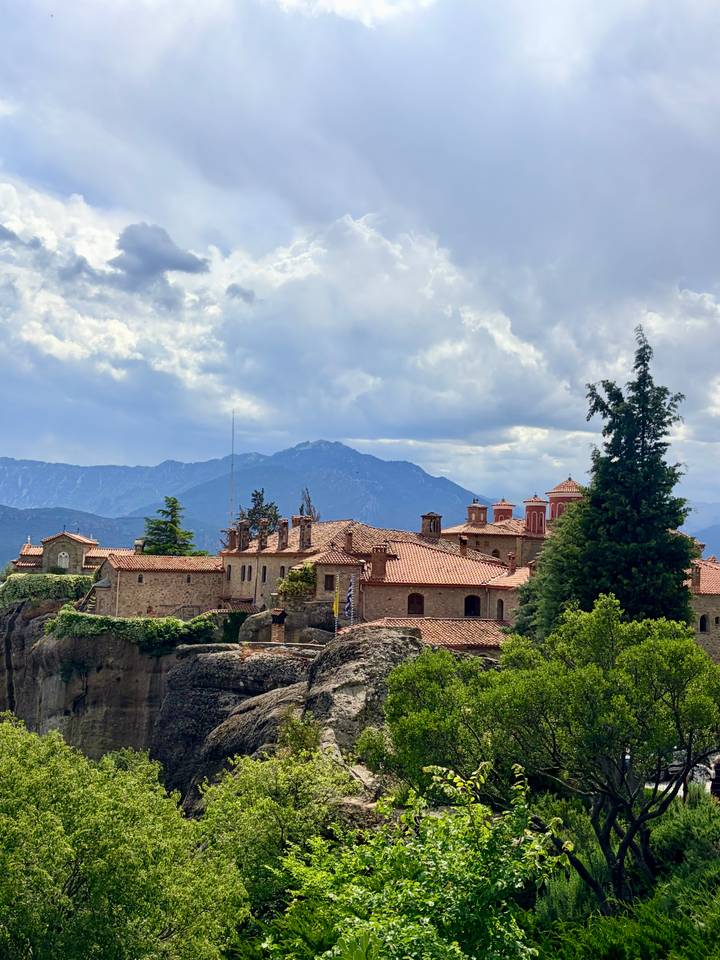 A hilltop monastery with terracotta roofs stands against a backdrop of distant blue mountains.