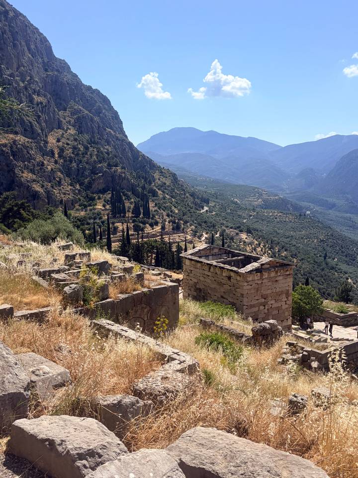Ruins of ancient Delphi cascade down a sun-drenched mountain slope with olive groves below.