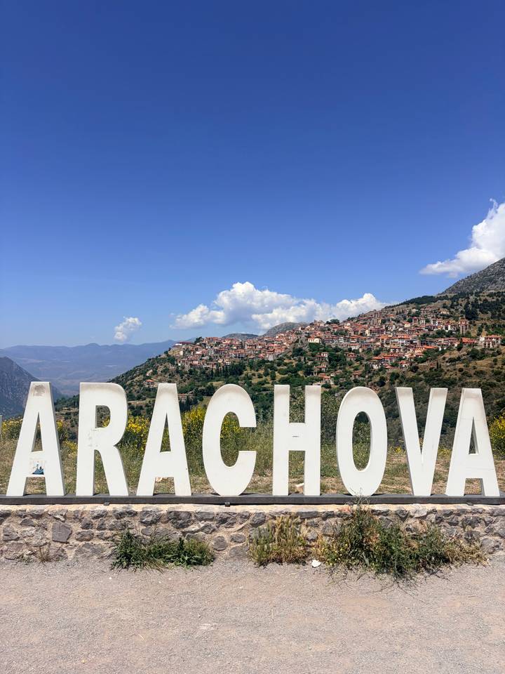 Large white letters spelling ARACHOVA overlook a hillside village and distant mountains under blue skies.