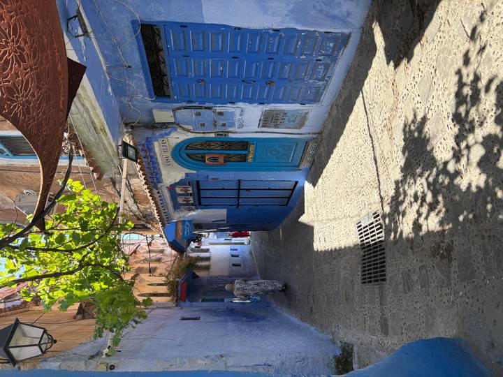 Shaded alley in Chefchaouen with blue doors, patterned awnings and a lone local walking.