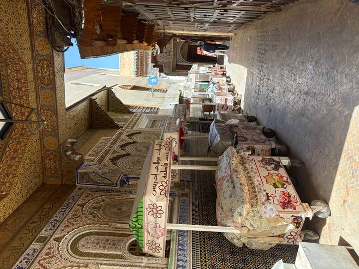 Sun-dappled corridor of ornate tiled stalls in Fes’s medina with a single shopper in the distance.