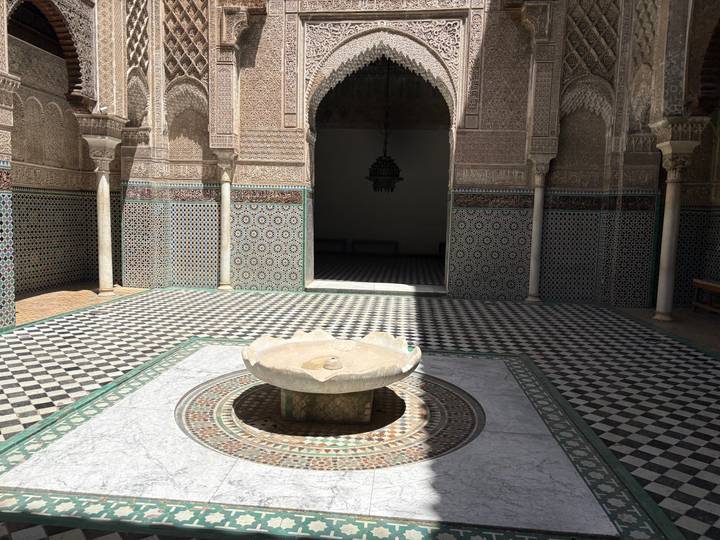 Quiet courtyard of a madrasa featuring geometric zellige tiles and a central marble fountain.